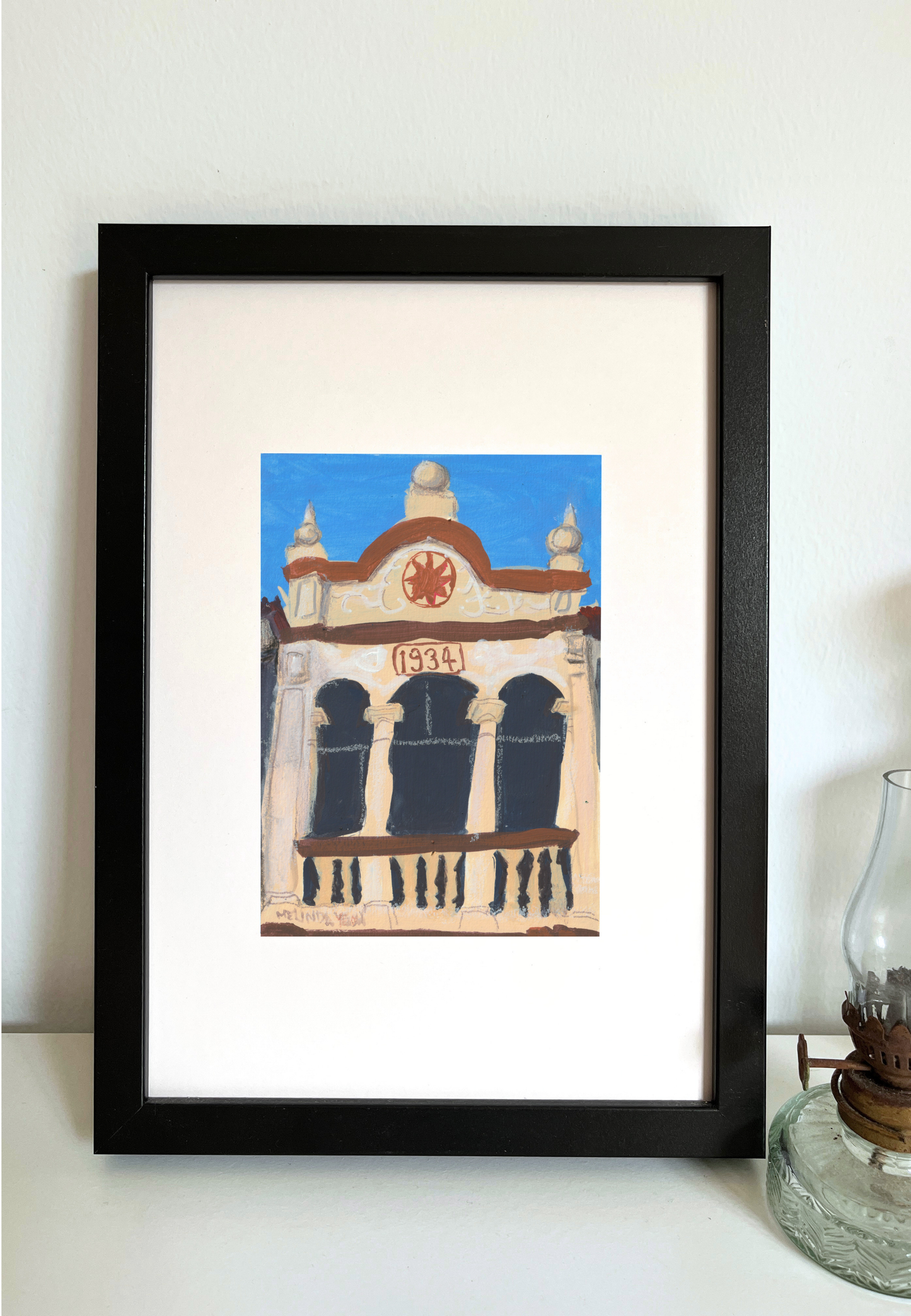 Framed painting of decorative architectural facade with '1934' and a red emblem on a blue sky background in Penang