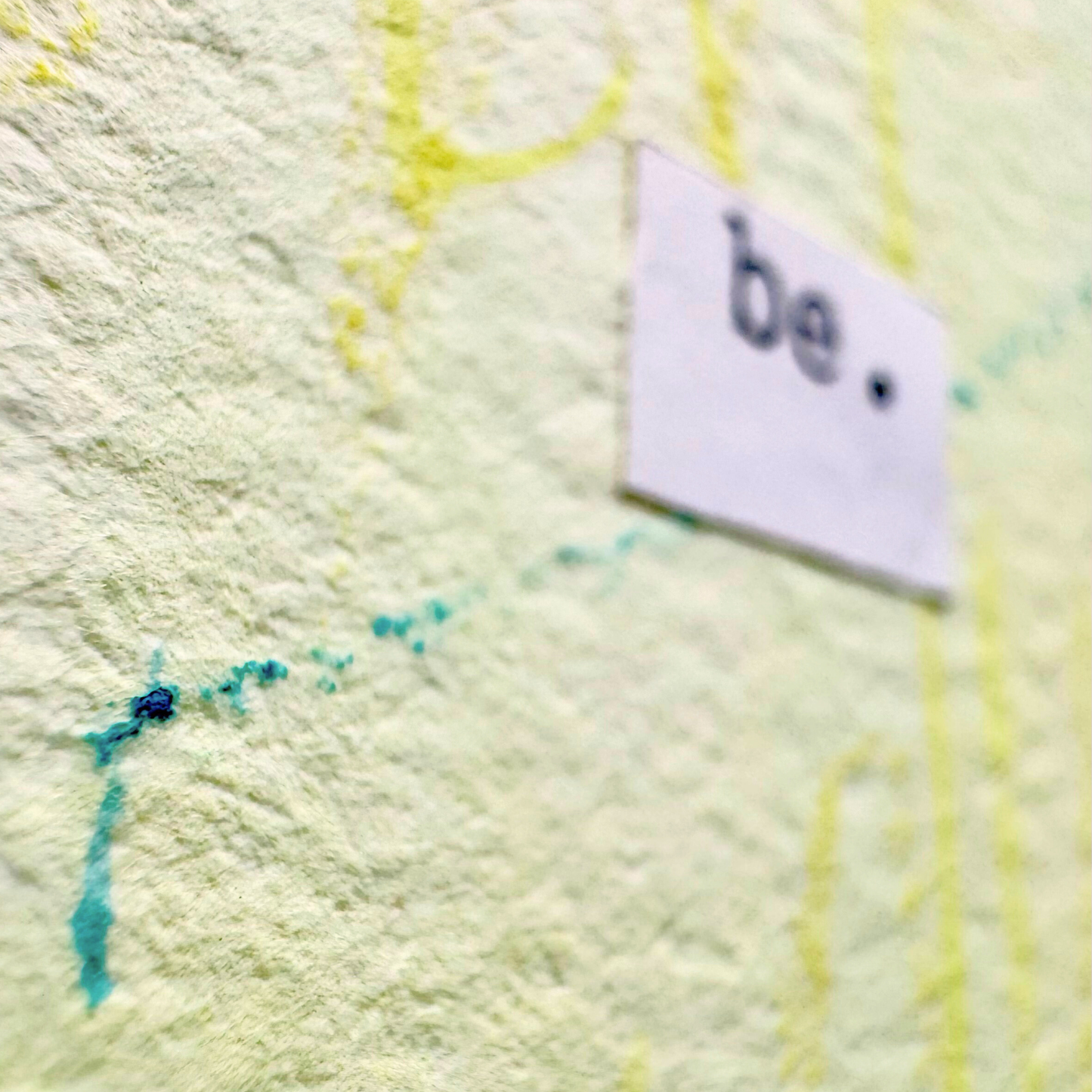 Close up of abstract mixed media painting with typewritten text 'be' on a textured cold pressed watercolour paper