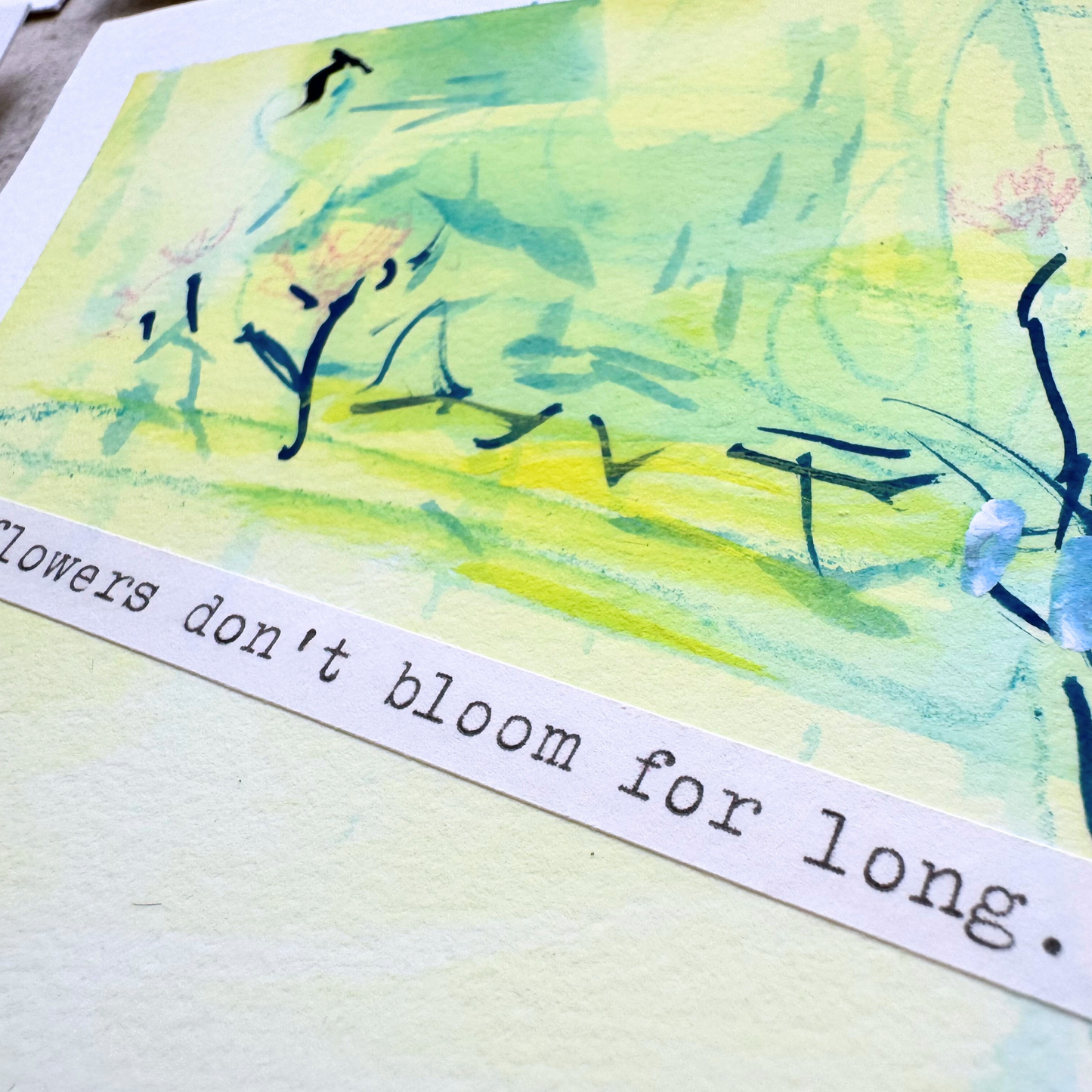 Close up of cheerful blue, green, yellow, pink abstract mixed media painting with flowers, typewritten text 'Flowers Don't Bloom For Long' on a smooth hot-pressed watercolour paper