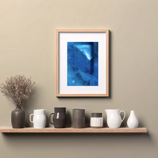 Framed abstract painting in blue with expressive brushstrokes and handwritten word Here I Am with a dot of red paint, spiritual modern art print, hanging on wall above a wooden counter top.
