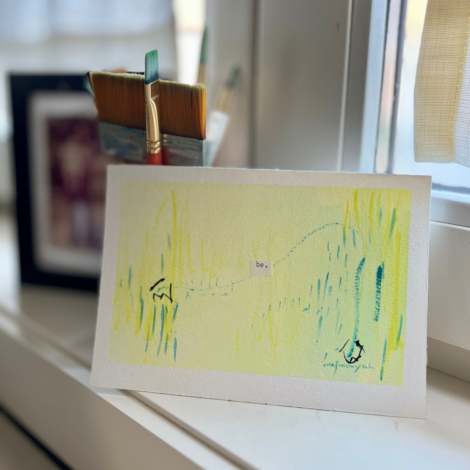 Abstract painting with typewriter word 'Be' and yellow and green abstract design on a white surface.