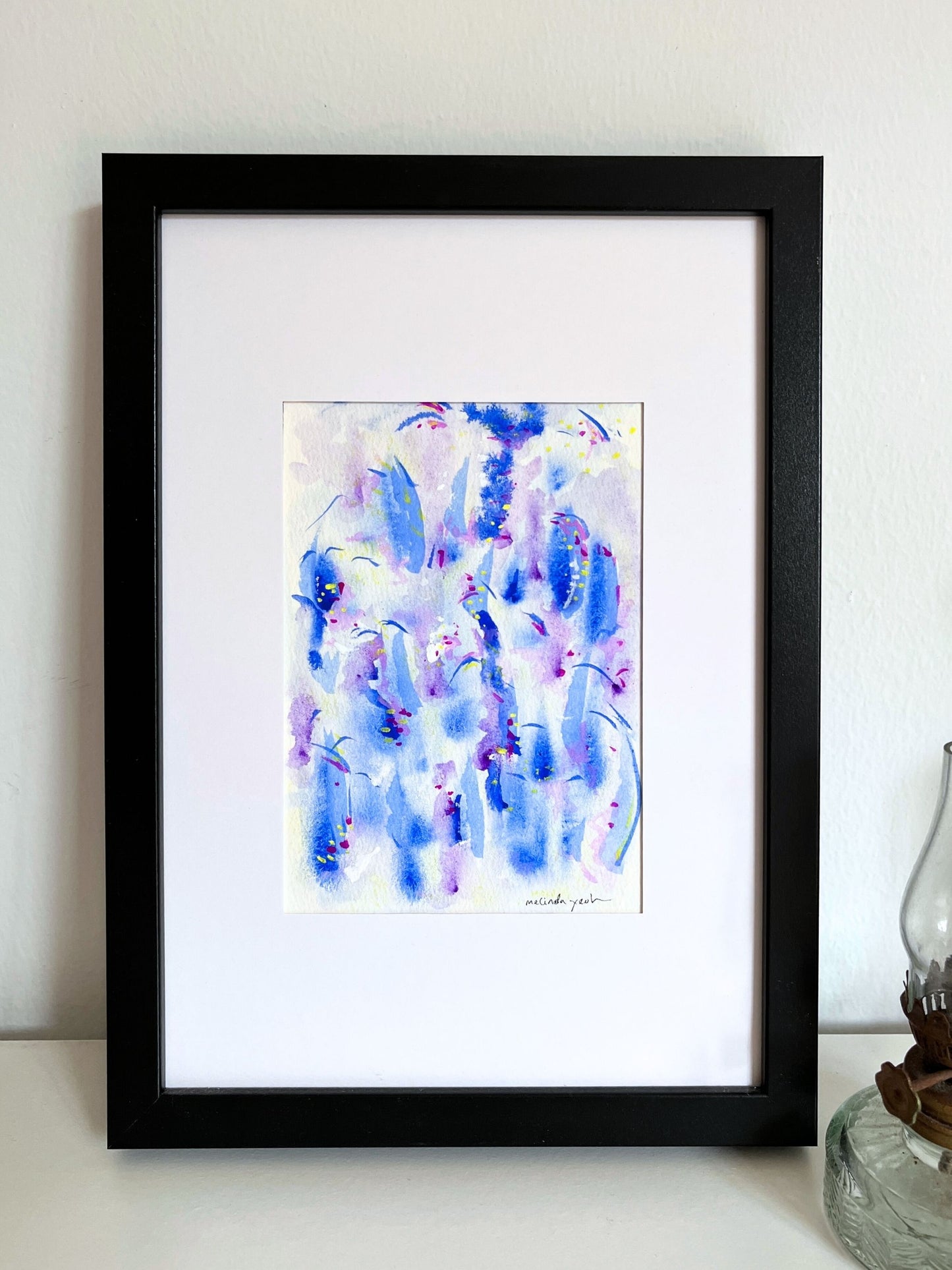 Framed abstract artwork with blue and purple hues on a white surface.