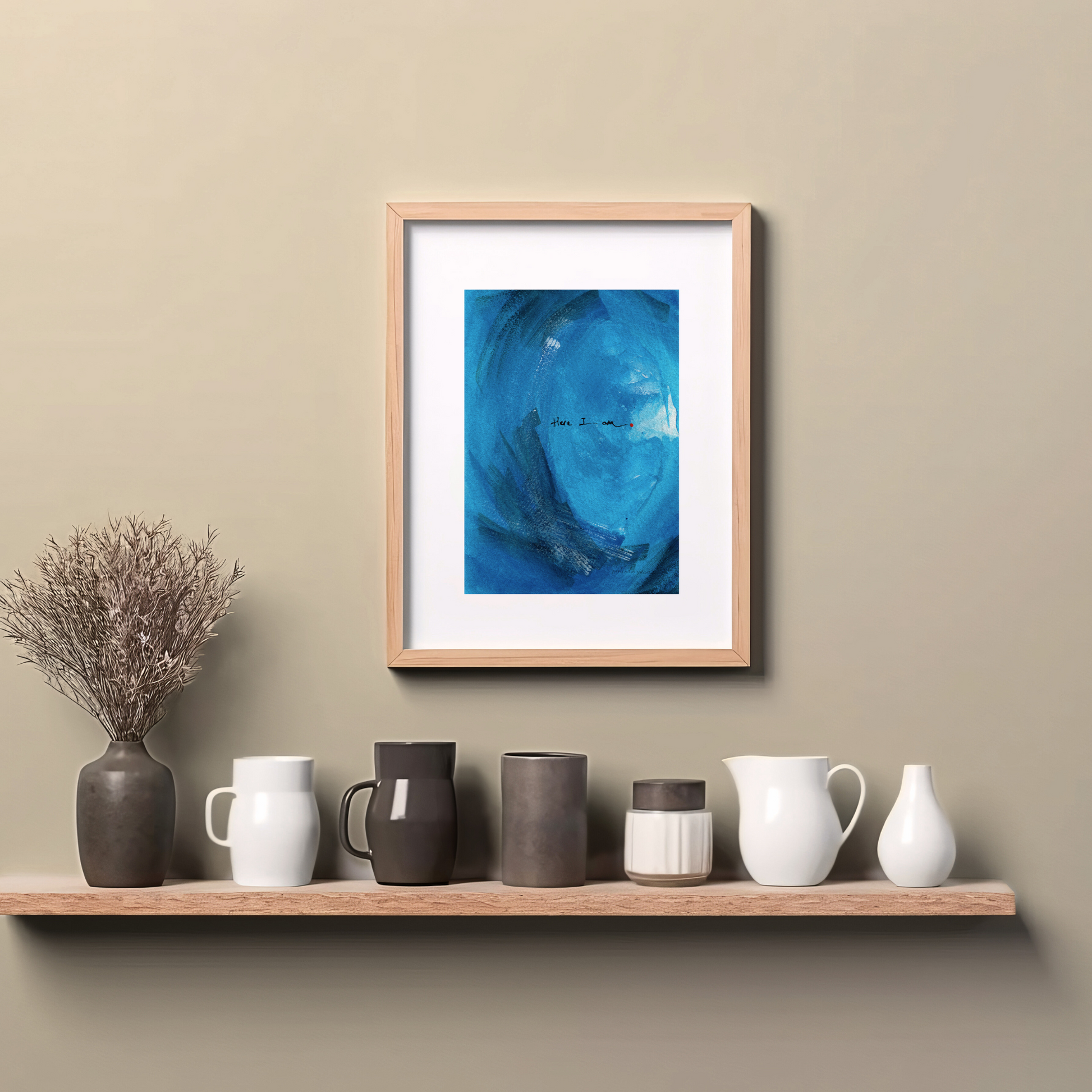 Framed abstract painting in blue with expressive brushstrokes and handwritten word Here I Am with a dot of red paint, spiritual modern art print, hanging on wall above a wooden counter top.