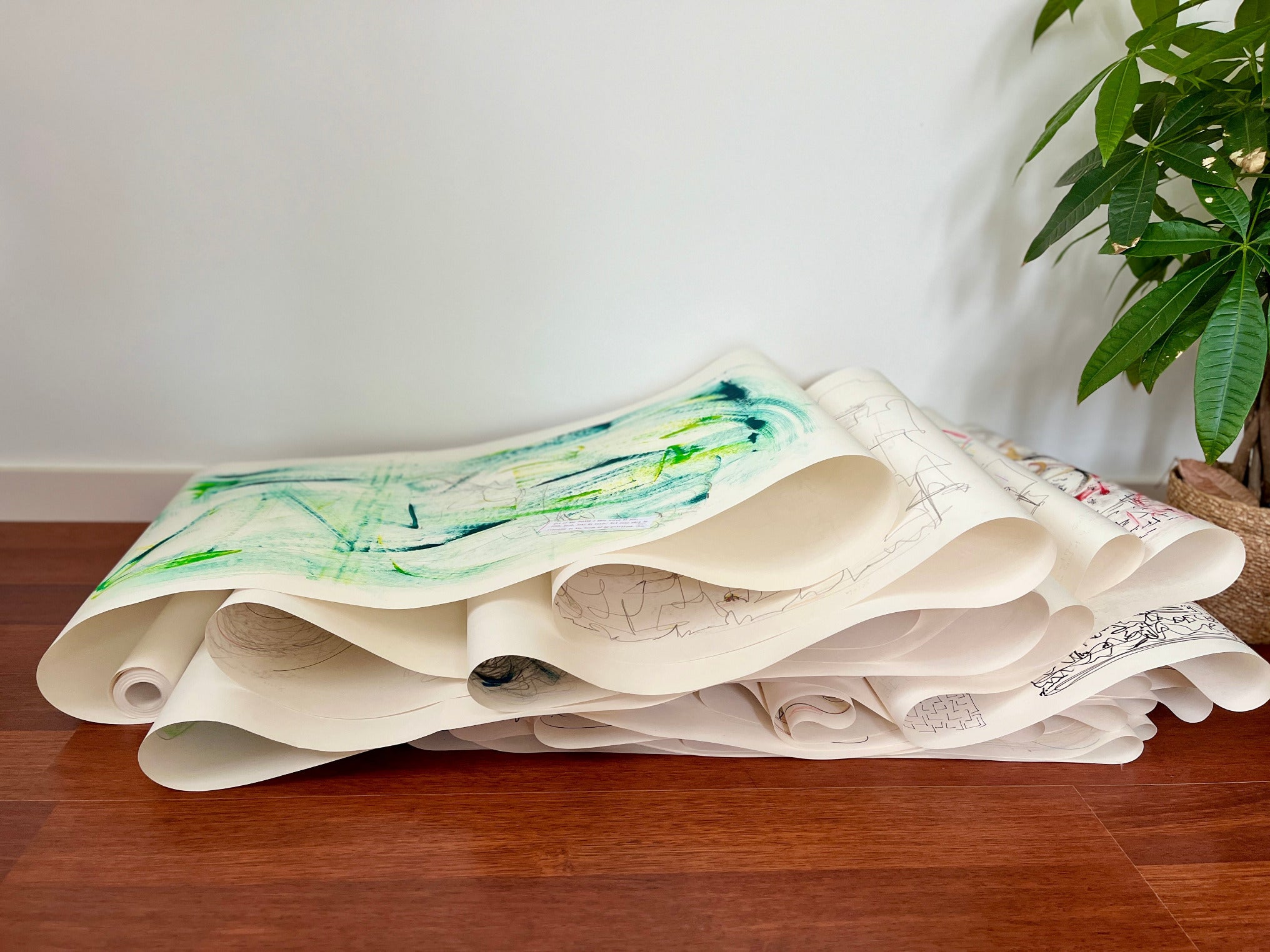 Stack of paper rolls with green and beige drawings on a wooden surface by Melinda Yeoh Art from monologue\worship/conversations series