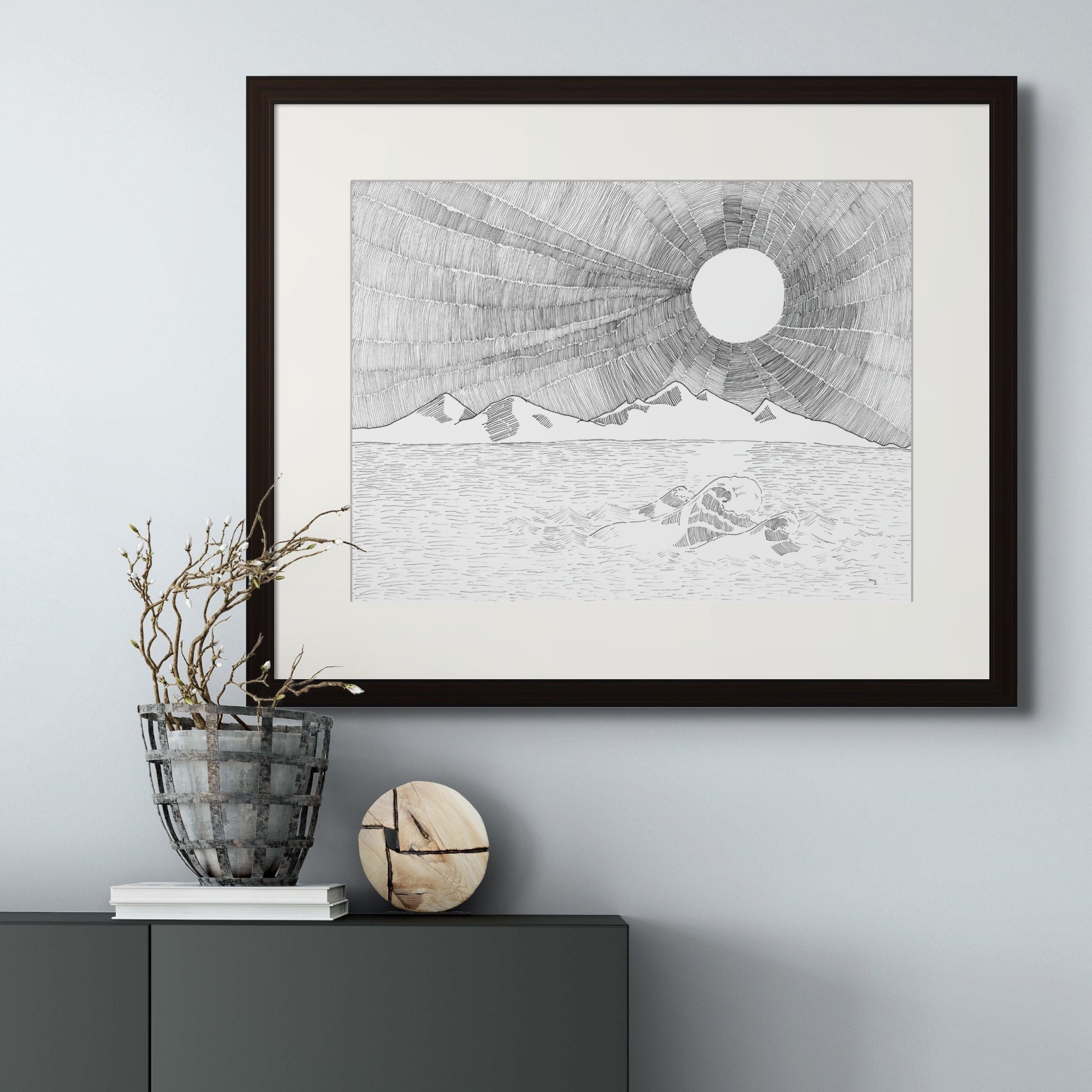 Image: line drawing giclée art print with black frame and cream colour mat of landscape scenery of sea, mountain and a magnificent sun